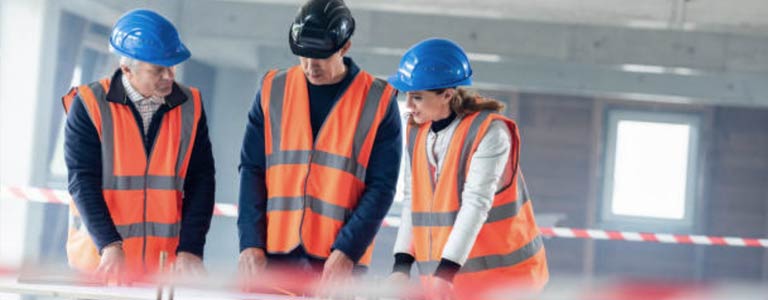 Specialist reviewing drawings on job site waering hard hemets and reflective vests