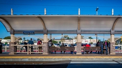Commuters at train stop under curved shade structure.