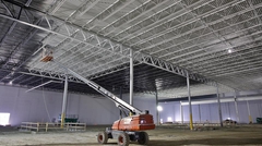 Steel joist and deck ceiling being painted after installation. Workers on a lift